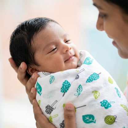 Newborn baby wrapped in a muslin swaddle blanket being held by a person with a blurred background