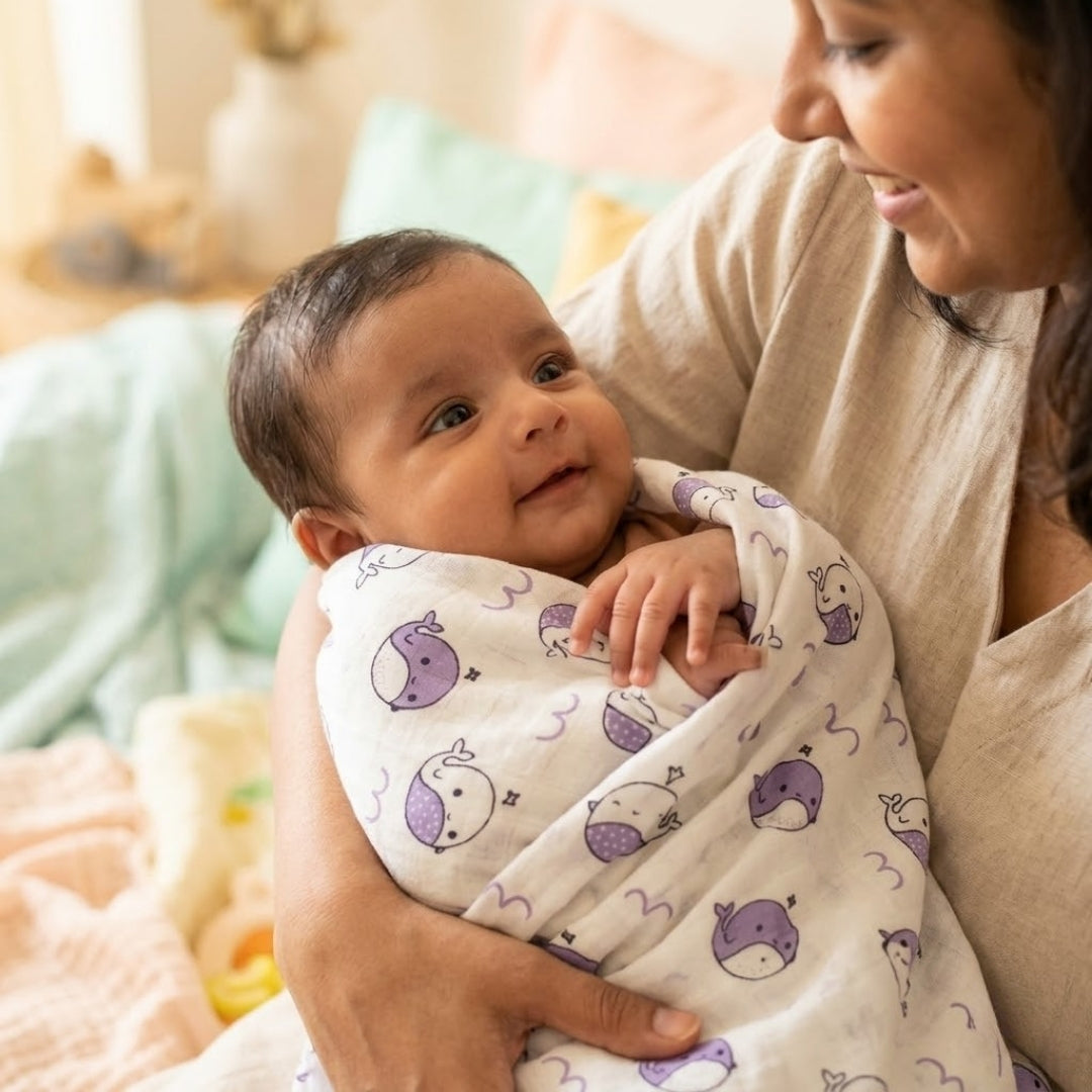 Woman holding a baby wrapped in a purple and white blanket with whale patterns.