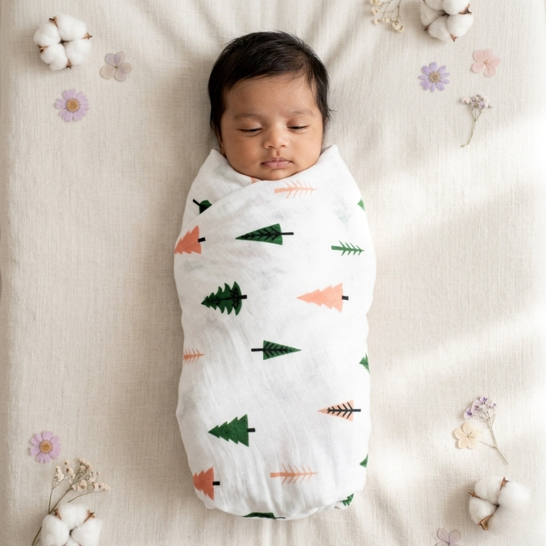 Newborn baby swaddled in a blanket with tree patterns, surrounded by cotton and flowers.