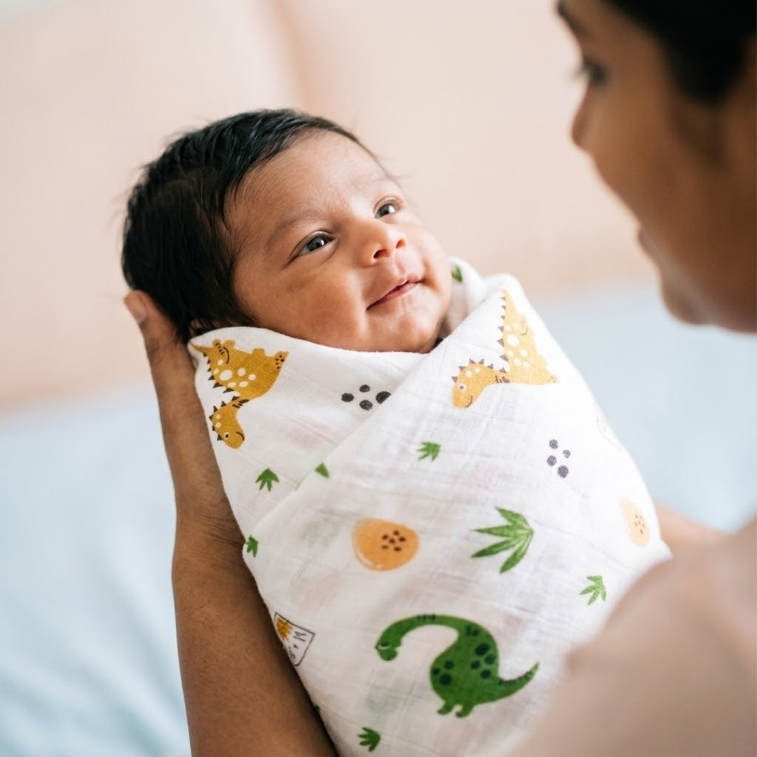 Baby wrapped in a dinosaur-patterned blanket being held by an adult.